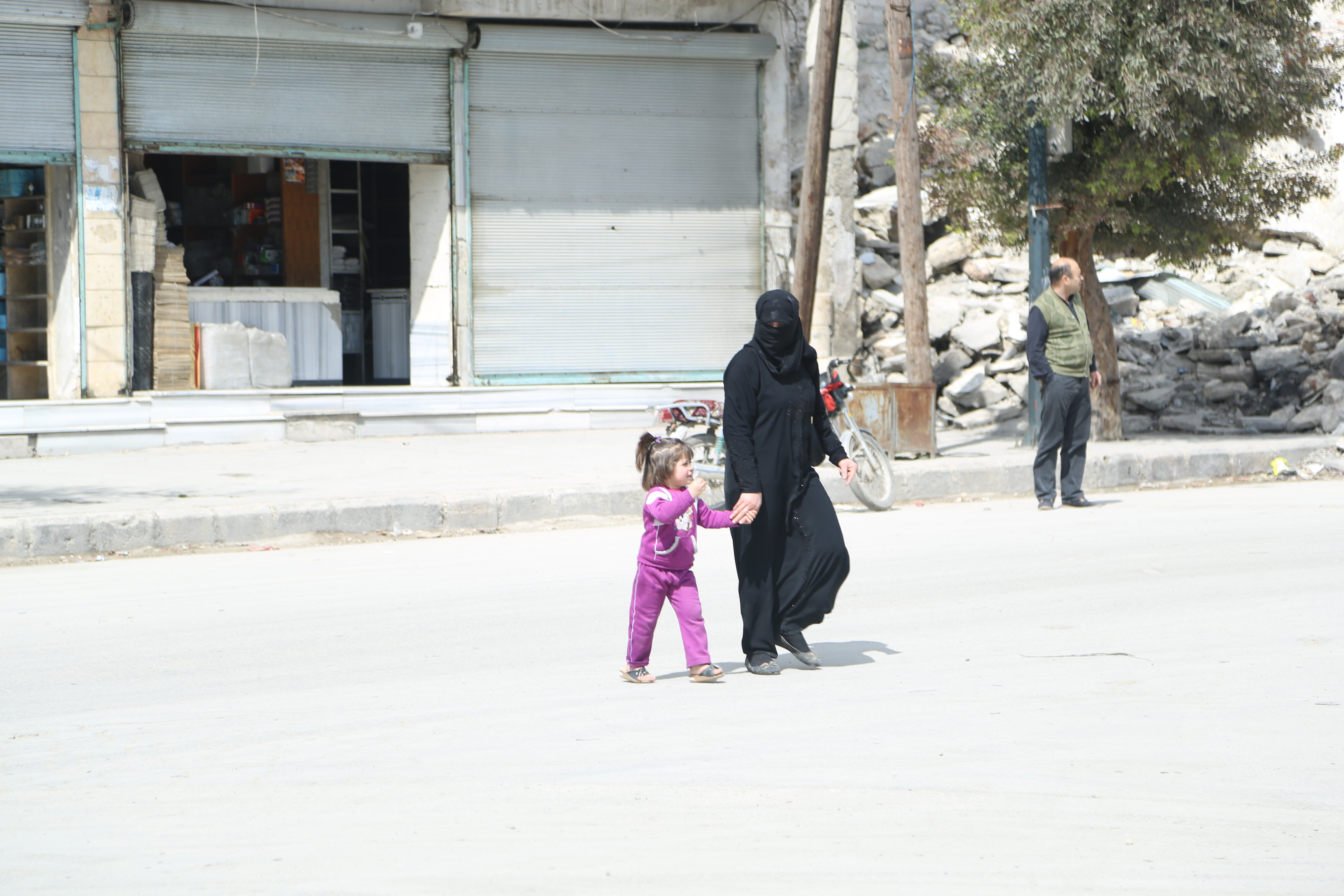 سيدة وطفلتها تقطع الشارع أمام مبنى مهدم في حي المرجة في حلب. تصوير حسام كويفاتية