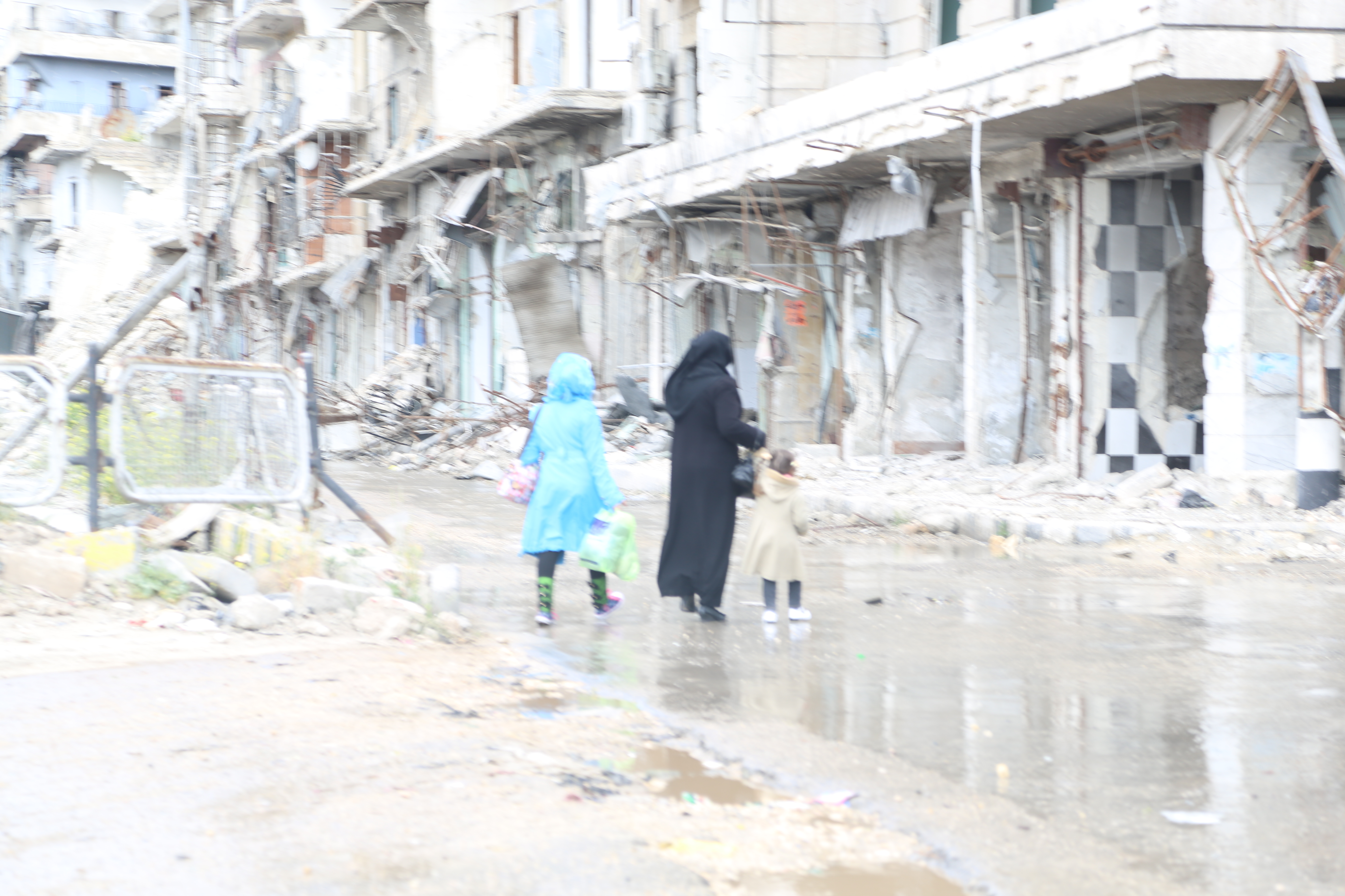 A woman and her children crossing the street in front of the remains of the al-Shaar bridge. Photo by: Hussam Kuwaifatiyeh